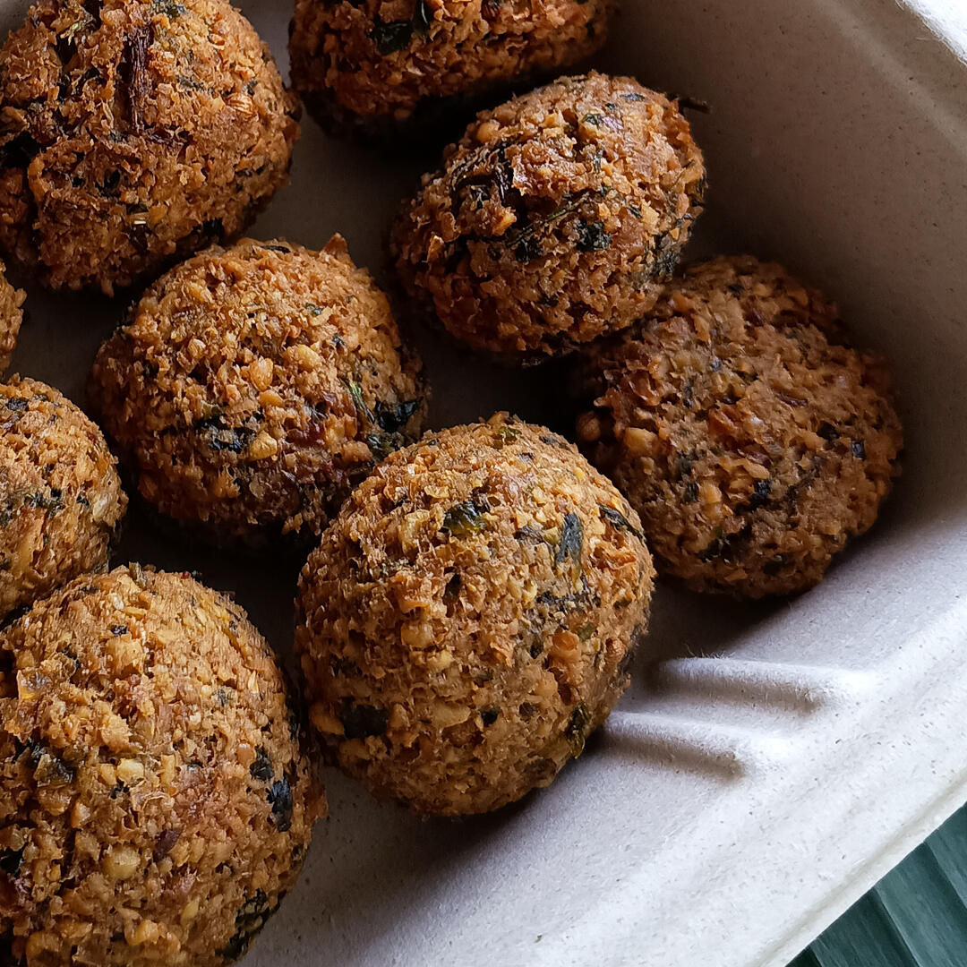 omicha-falafel-cha-gelado-sucos-naturais-omicha Uma mão segurando três cenouras frescas com suas ramas verdes vibrantes, apoiadas sobre uma cama de alface crespa verde-escura. A imagem foca na pureza e frescor dos ingredientes naturais da Omicha, promovendo a alimentação consciente no bairro Dionísio To